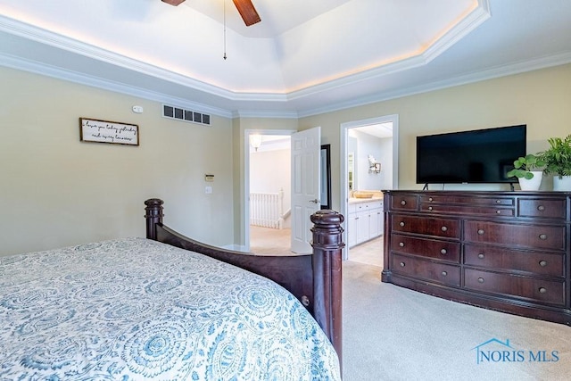 bedroom featuring ceiling fan, ensuite bathroom, ornamental molding, light colored carpet, and a raised ceiling