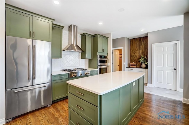 kitchen with stainless steel appliances, green cabinets, decorative backsplash, and wall chimney exhaust hood