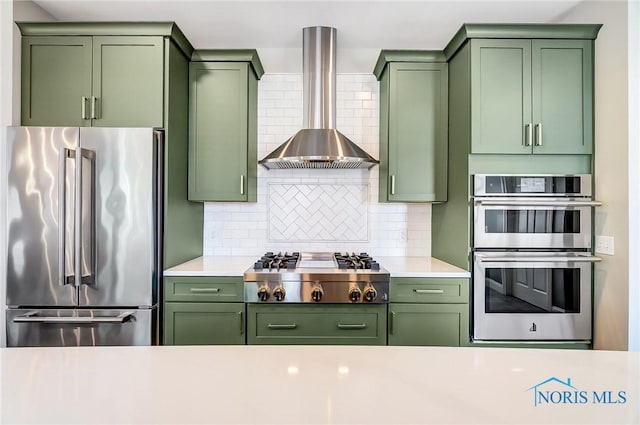 kitchen with tasteful backsplash, stainless steel appliances, wall chimney exhaust hood, and green cabinets