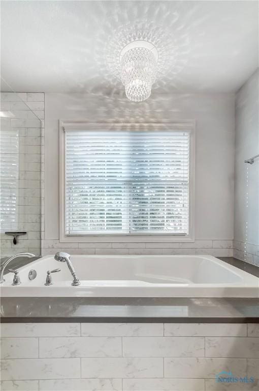 bathroom featuring tiled tub, plenty of natural light, and a notable chandelier