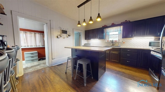 kitchen featuring a kitchen island, pendant lighting, sink, dark hardwood / wood-style flooring, and a kitchen bar