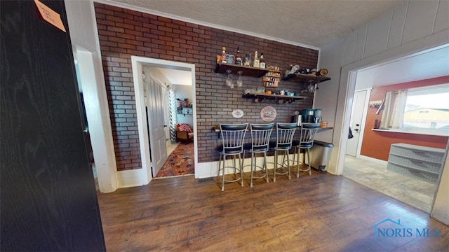 bar with ornamental molding, brick wall, dark hardwood / wood-style floors, and a textured ceiling