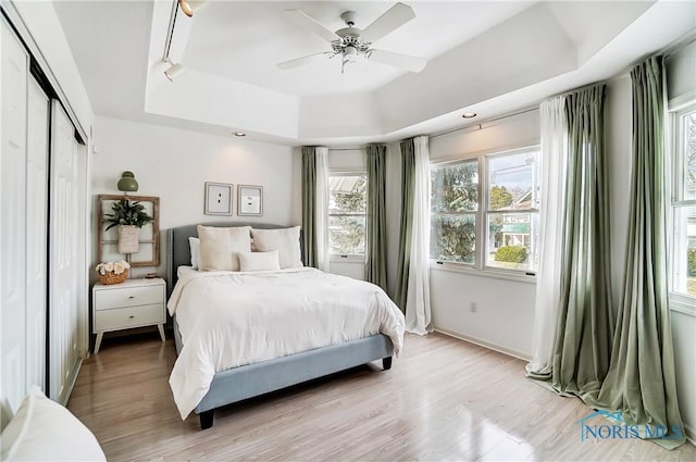 bedroom featuring a raised ceiling, light hardwood / wood-style floors, ceiling fan, and a closet