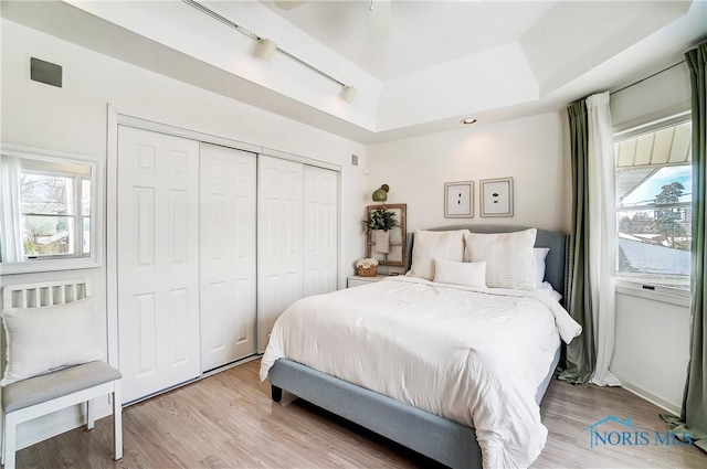 bedroom with rail lighting, a closet, ceiling fan, a raised ceiling, and light hardwood / wood-style flooring