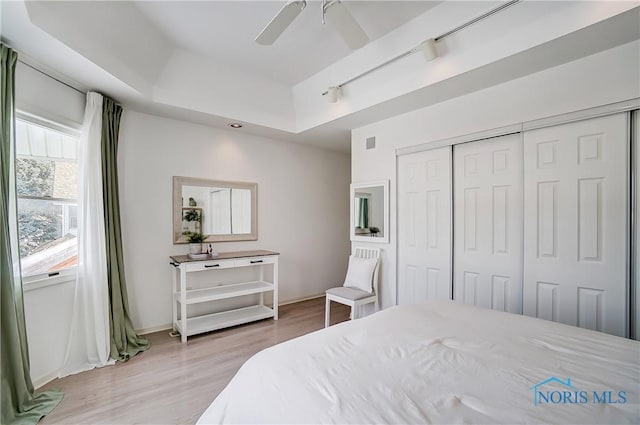 bedroom featuring a raised ceiling, light wood-type flooring, ceiling fan, and a closet