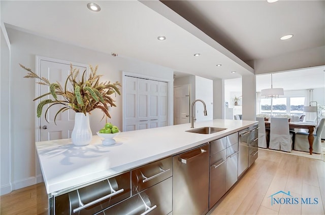 kitchen featuring dishwasher, sink, a center island with sink, and light wood-type flooring