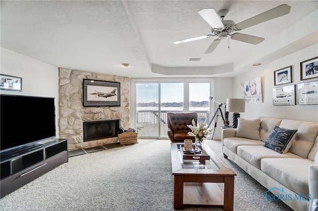 living room with a textured ceiling, a tray ceiling, carpet floors, ceiling fan, and a fireplace