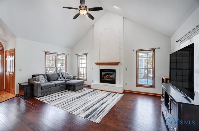 living room featuring dark wood-type flooring, a healthy amount of sunlight, a fireplace, and high vaulted ceiling