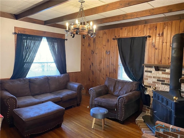 living room with dark hardwood / wood-style floors, wood walls, a wood stove, a chandelier, and beam ceiling