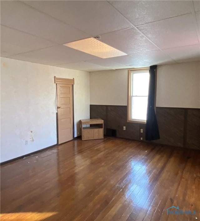 empty room with dark hardwood / wood-style floors and a drop ceiling