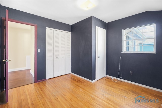 unfurnished bedroom featuring lofted ceiling, wood-type flooring, and a closet