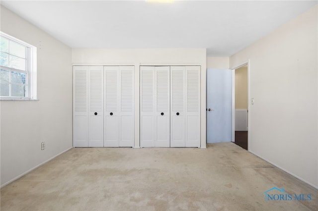 unfurnished bedroom featuring multiple closets and light carpet