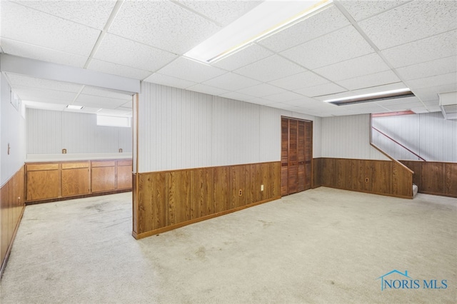 basement with a paneled ceiling and light colored carpet