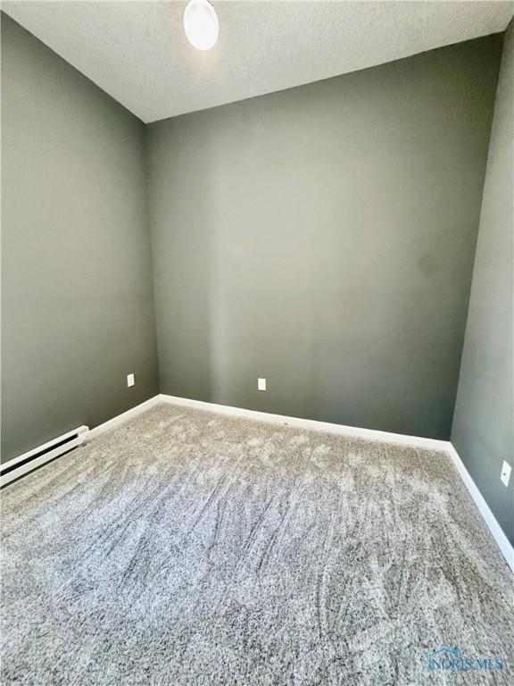 spare room with a baseboard heating unit, a textured ceiling, and carpet