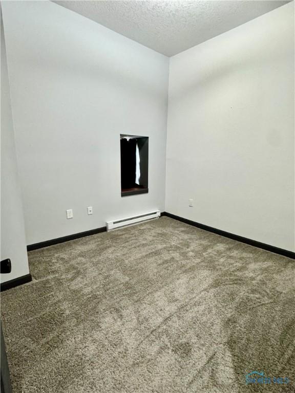 carpeted empty room with a baseboard radiator and a textured ceiling