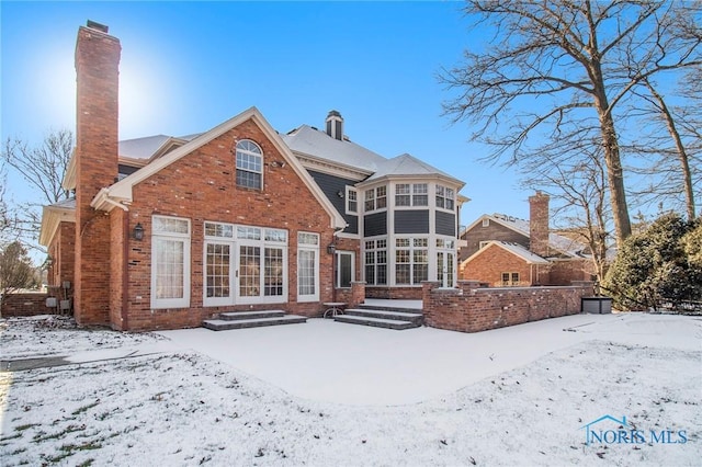 snow covered rear of property with a sunroom