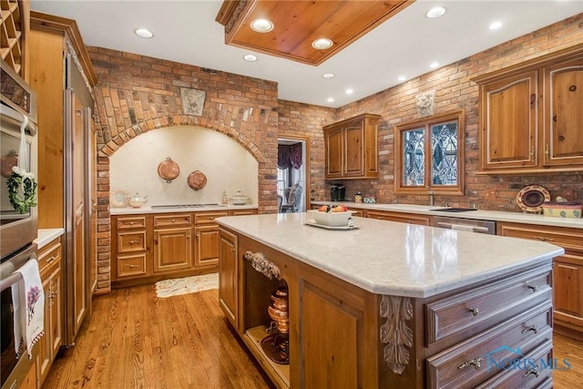 kitchen featuring a kitchen island, stainless steel appliances, light hardwood / wood-style floors, brick wall, and decorative backsplash