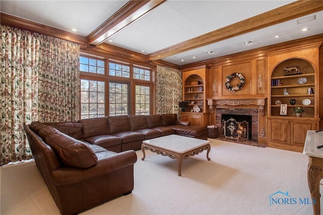 living room featuring built in shelves, a stone fireplace, crown molding, light colored carpet, and beam ceiling