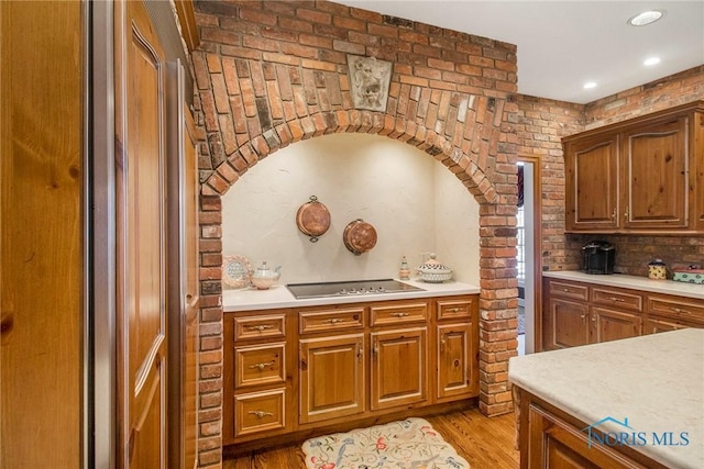 kitchen featuring black electric cooktop, backsplash, brick wall, and light wood-type flooring