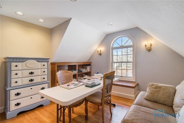 home office with lofted ceiling, light hardwood / wood-style floors, and a textured ceiling