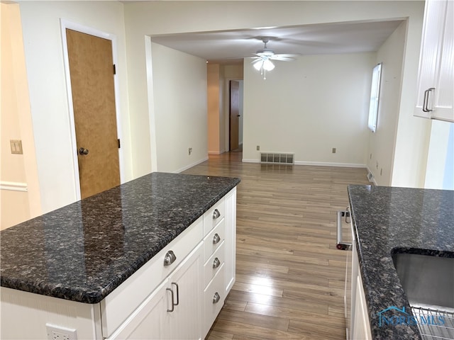 kitchen featuring hardwood / wood-style flooring, a center island, dark stone countertops, and white cabinets