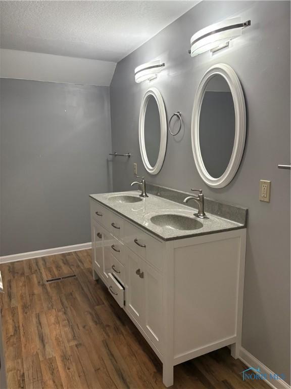 bathroom featuring vaulted ceiling, hardwood / wood-style floors, vanity, and a textured ceiling