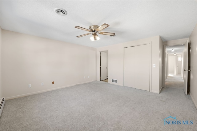 unfurnished bedroom featuring light carpet, a baseboard heating unit, a closet, and ceiling fan