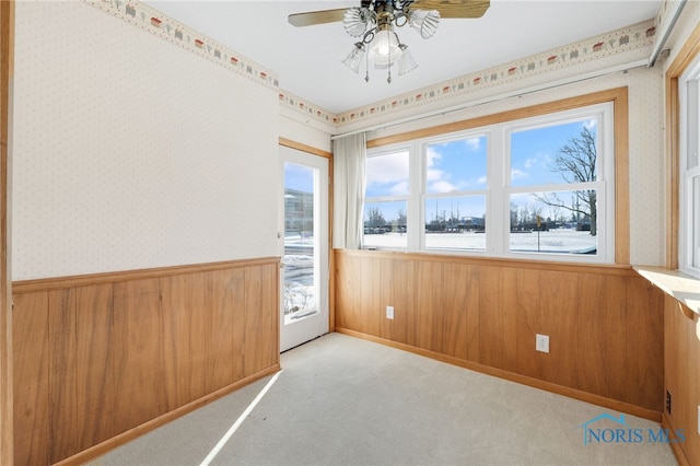 empty room with plenty of natural light, light carpet, ceiling fan, and wood walls