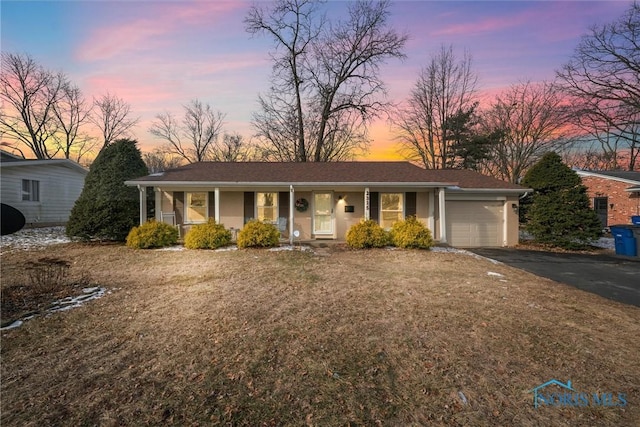 ranch-style house with a garage, covered porch, and a lawn