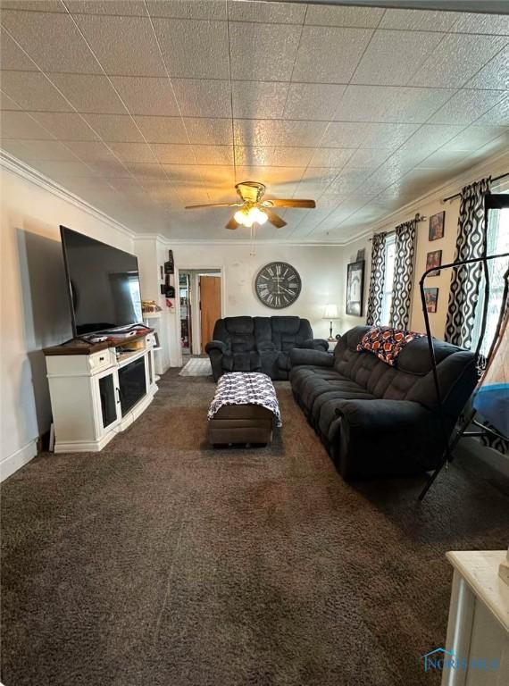 living room with dark colored carpet, ornamental molding, and ceiling fan