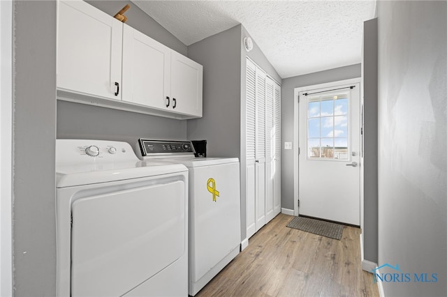 laundry area with a textured ceiling, light hardwood / wood-style floors, cabinets, and washing machine and clothes dryer