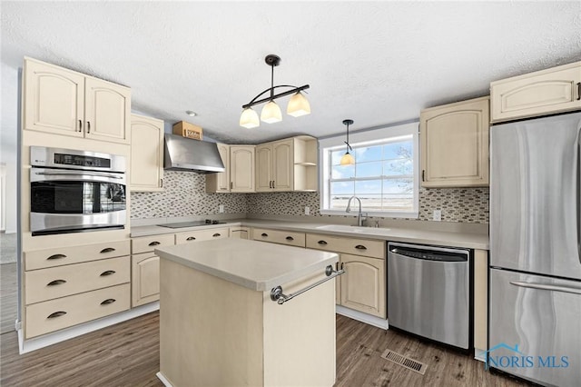 kitchen with sink, stainless steel appliances, a kitchen island, decorative light fixtures, and wall chimney exhaust hood