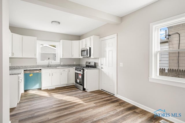 kitchen with white cabinetry, sink, light hardwood / wood-style floors, stainless steel appliances, and beam ceiling