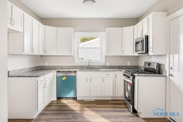 kitchen with appliances with stainless steel finishes, sink, white cabinets, light stone countertops, and dark wood-type flooring