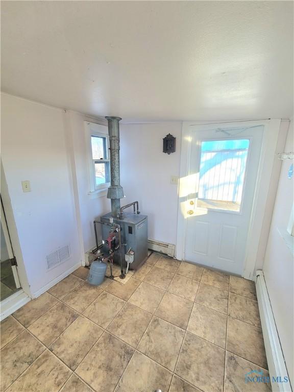 interior space with plenty of natural light, a wood stove, and baseboard heating