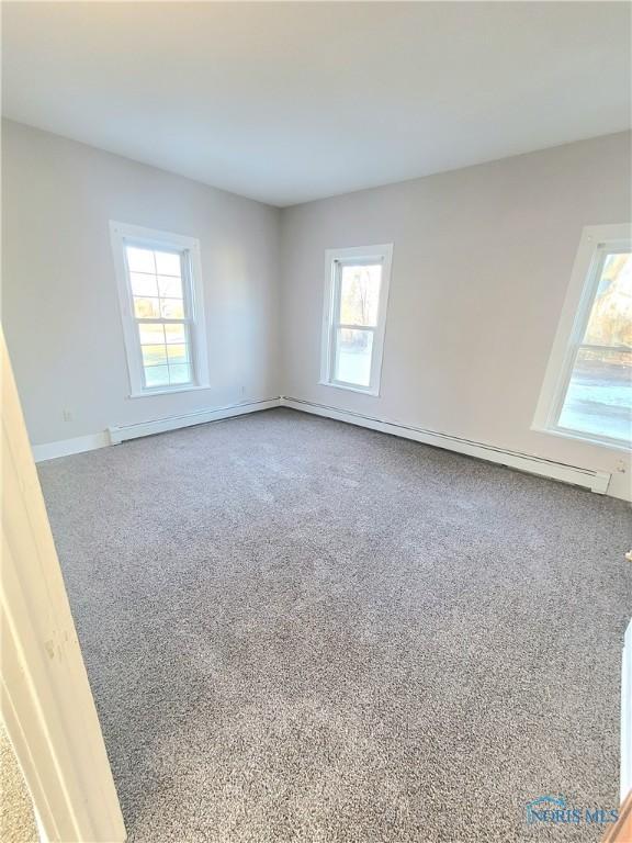 empty room with a baseboard heating unit, carpet floors, and a wealth of natural light