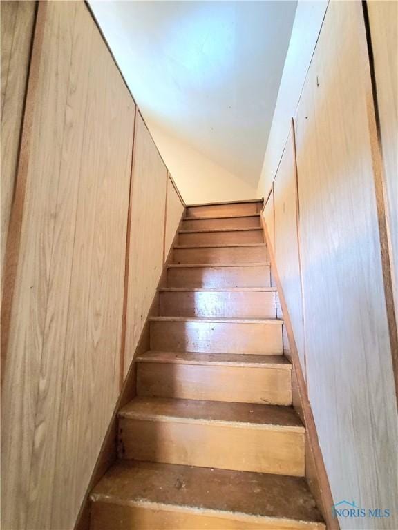 stairway featuring vaulted ceiling and wooden walls