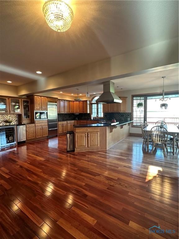 kitchen with appliances with stainless steel finishes, pendant lighting, dark hardwood / wood-style flooring, a chandelier, and island exhaust hood