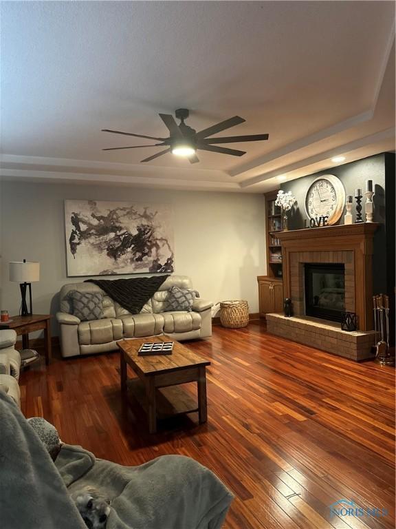 living room featuring ceiling fan, a fireplace, a raised ceiling, and hardwood / wood-style floors