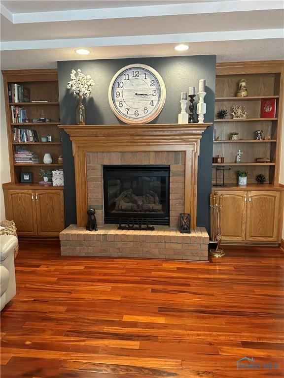 living room with a brick fireplace, built in features, and dark hardwood / wood-style flooring