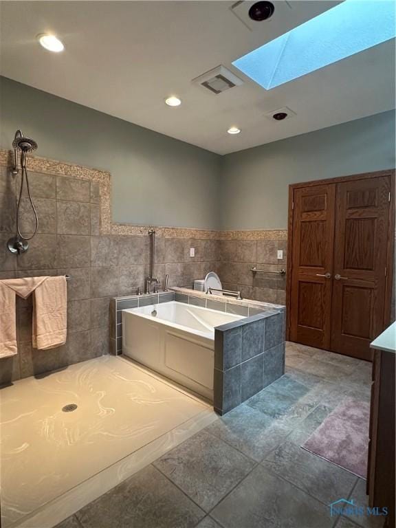 bathroom with a skylight, vanity, a bathing tub, and tile walls