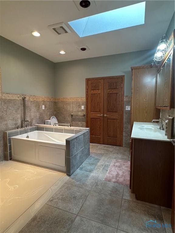 bathroom featuring a bathing tub, tile walls, vanity, and a skylight