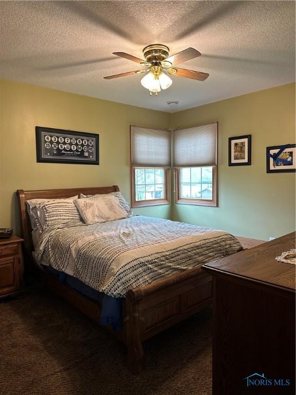 bedroom featuring ceiling fan, dark carpet, and a textured ceiling