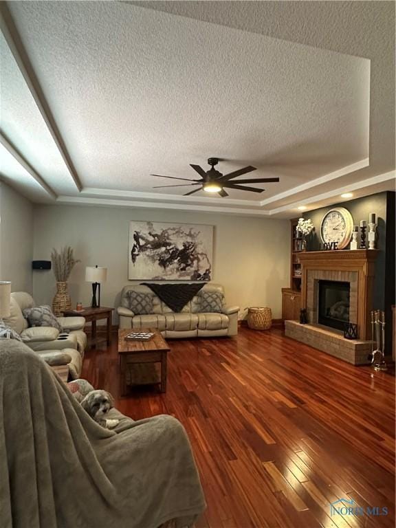 living room featuring ceiling fan, a tray ceiling, wood-type flooring, a textured ceiling, and a tiled fireplace