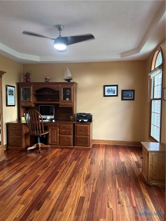 unfurnished office featuring dark hardwood / wood-style floors, a raised ceiling, and a textured ceiling