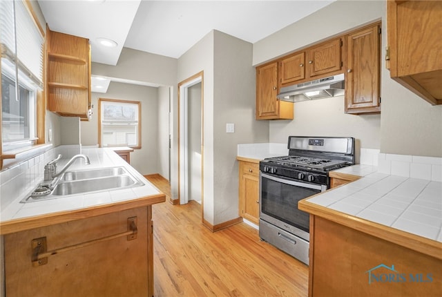 kitchen with gas range, tile countertops, light hardwood / wood-style floors, and sink