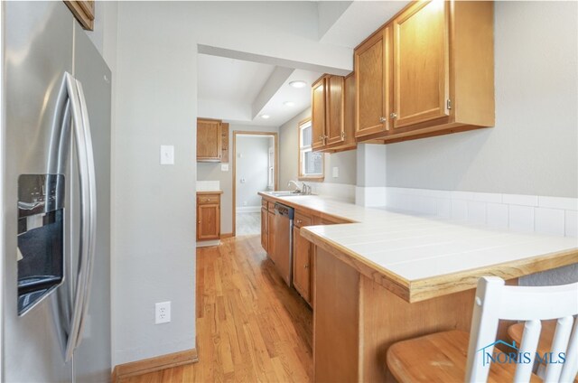 kitchen with appliances with stainless steel finishes, sink, a breakfast bar area, kitchen peninsula, and light hardwood / wood-style flooring