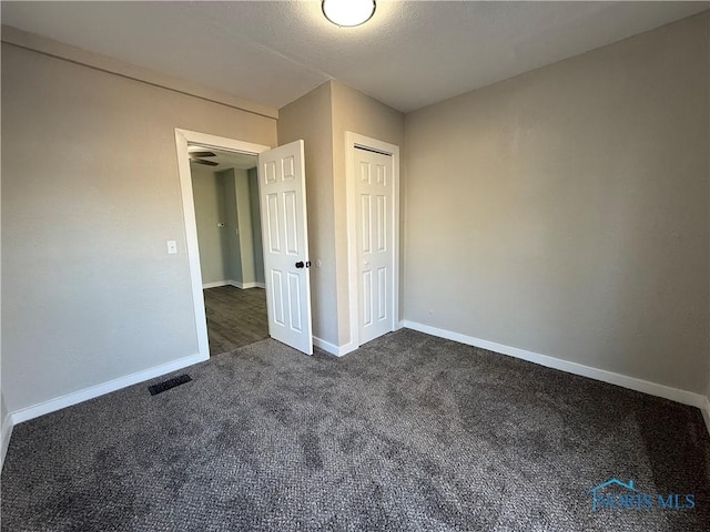 unfurnished bedroom with a closet, a textured ceiling, and dark colored carpet