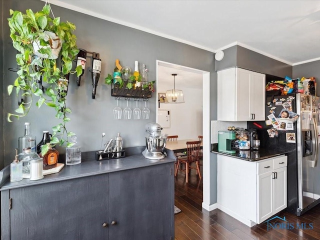 kitchen with dark wood-type flooring, white cabinetry, stainless steel refrigerator with ice dispenser, ornamental molding, and decorative light fixtures