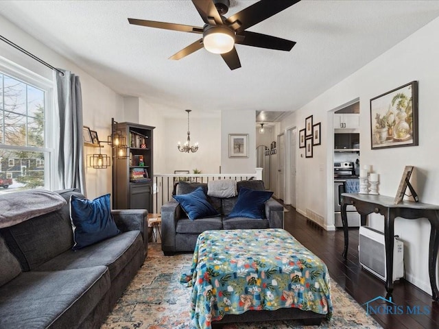 living room featuring dark hardwood / wood-style flooring, ceiling fan with notable chandelier, and a textured ceiling